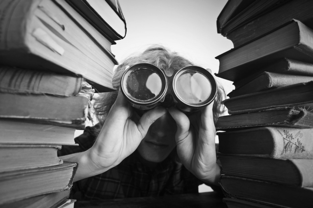 Mann schaut mit Gucker zwischen Stapel Bücher hervor
