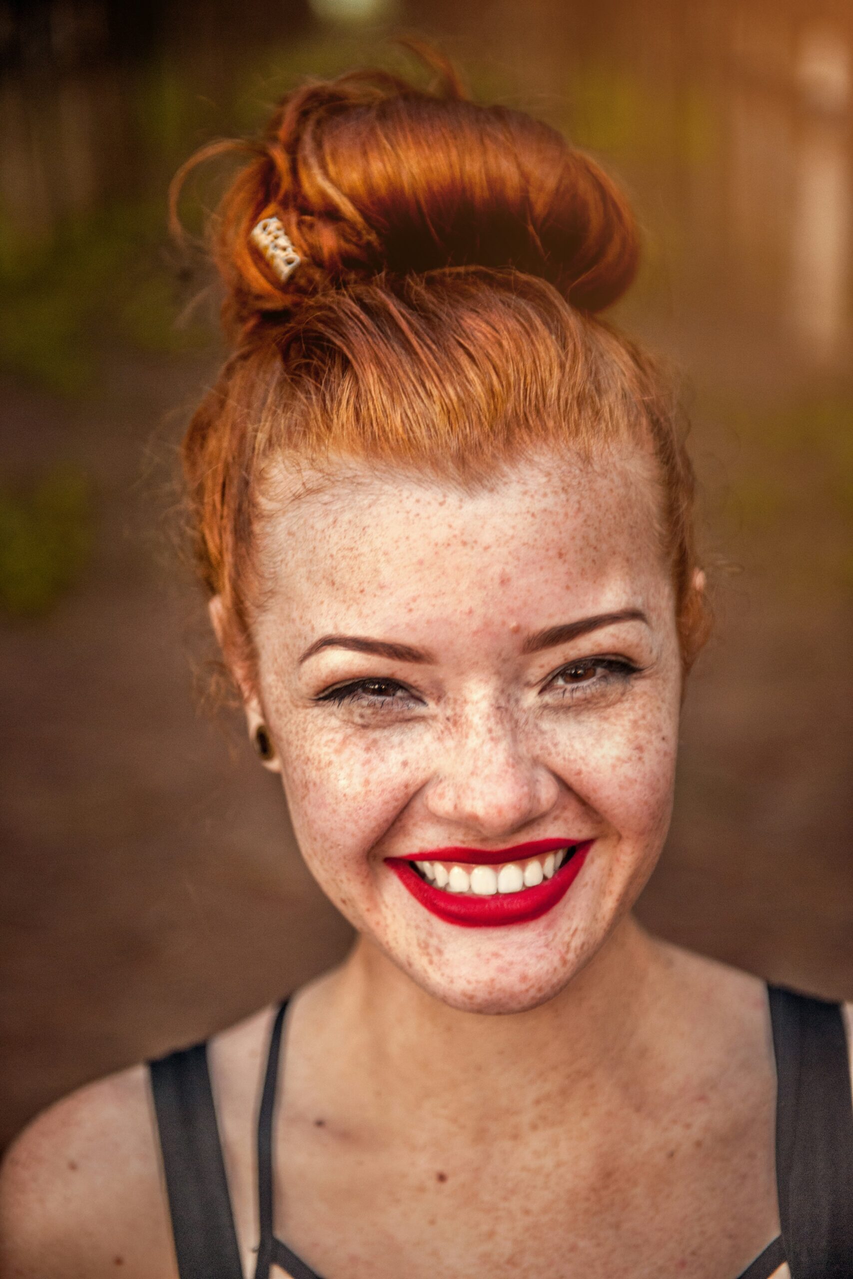 Junge Frau mit orangenen Haaren, Sommersprossen und einem roten Lippenstift lächelt in die Kamera